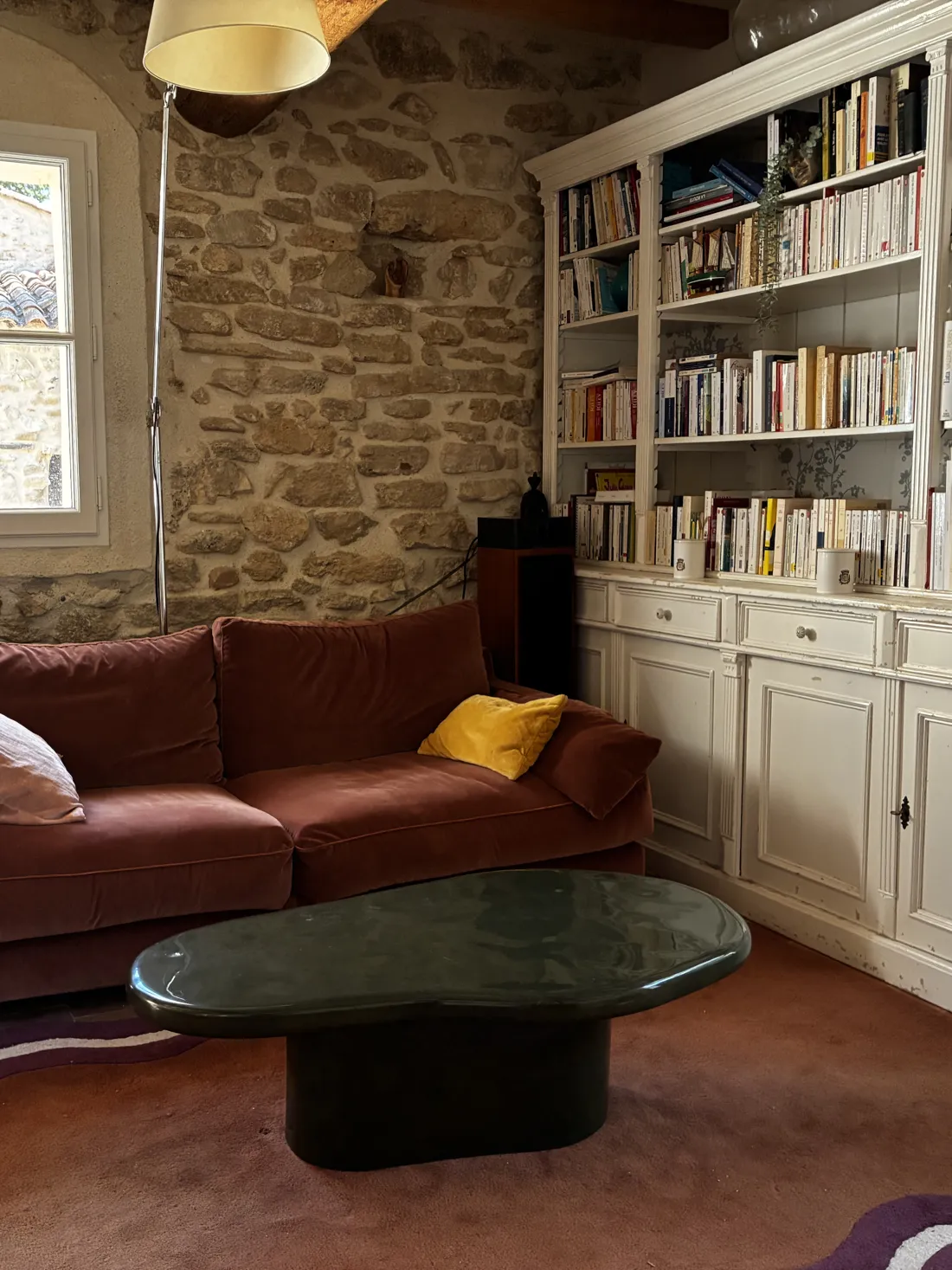 Bibliothèque, canapé en velours et mur de pierre apparente dans un mas provençal rénové